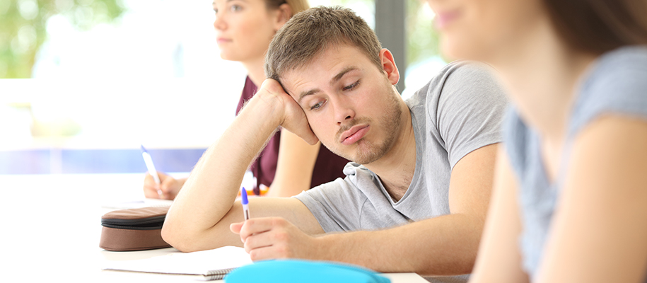White male in grey T-shirt looking bored in class between two White females