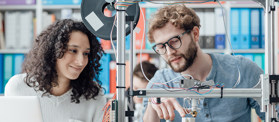 Curly haired woman with man in glasses observing engineering machine in class