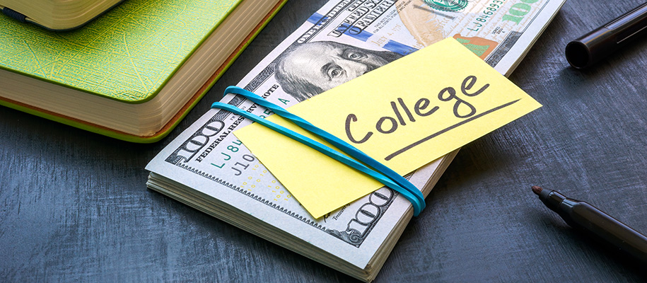 Bundle of hundred bills in band with note saying college next to notebooks