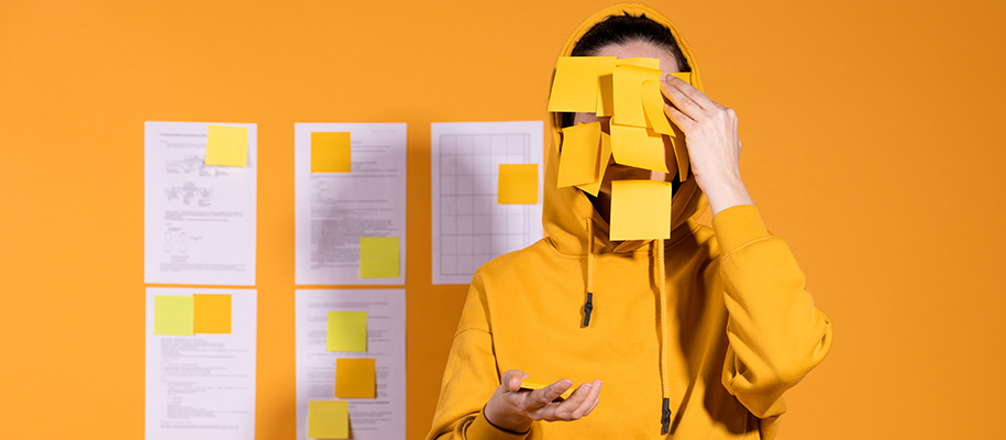 Person stands by project wall in yellow sweatshirt putting Post Its on face