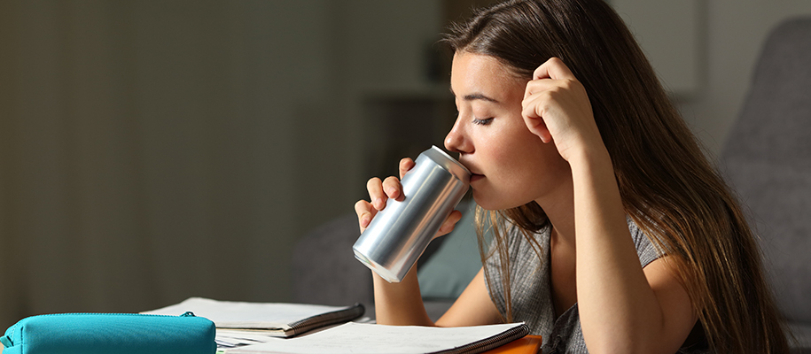 Young woman with long brown hair, studying, tired, drinking from unmarked soda
