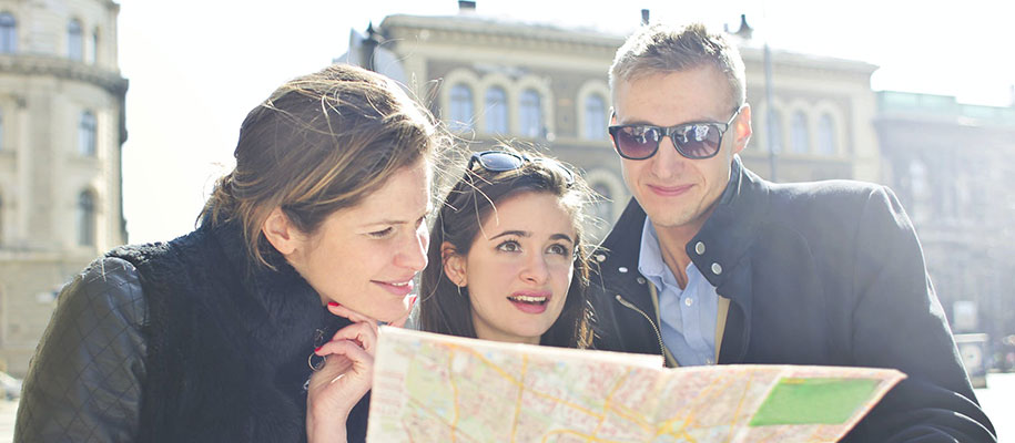 Two women and a man huddled and reading a map in a city