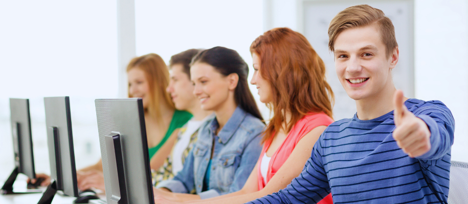 Group of five students at computers, focus on White male giving thumbs up