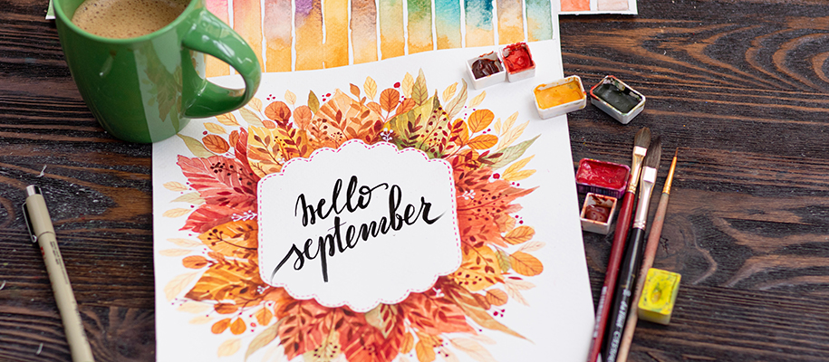 Paper painted with fall leaves and Hello September surrounded by coffee and pain