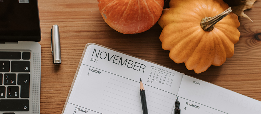 November calendar planner next to laptop and small pumpkins on a wooden desk