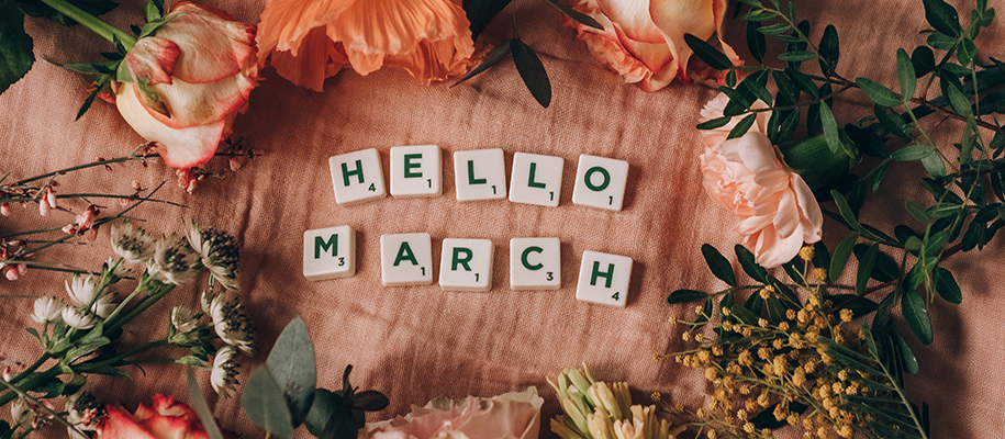 Pink flowers laid out on pink sheets with Scrabble tiles spelling Hello March