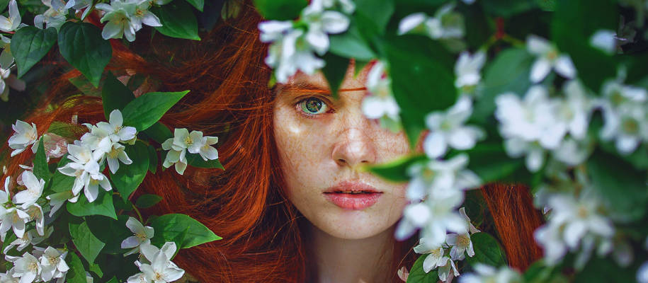 White red-headed girl hiding in bush of white flowers looking shy