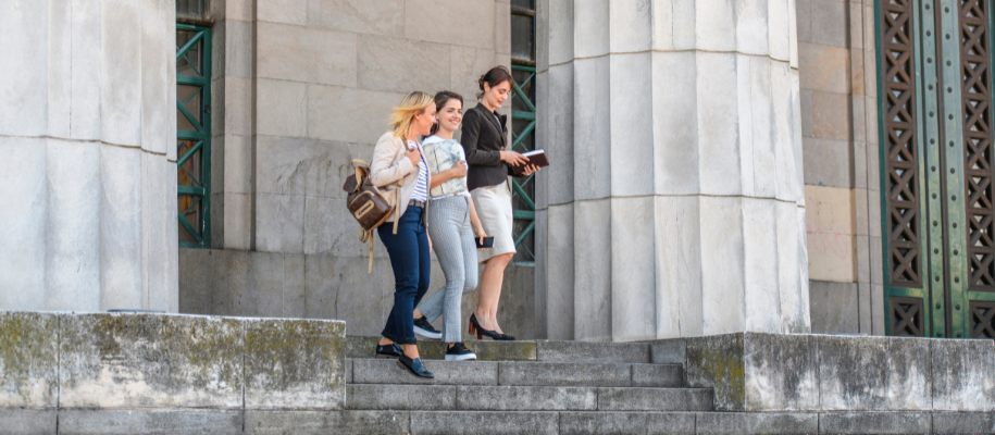 Three young woman in business casual attire with books and bag on stone steps