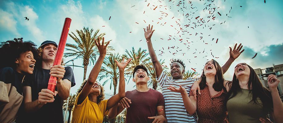 Group of diverse, excited college students using confetti cannon outside