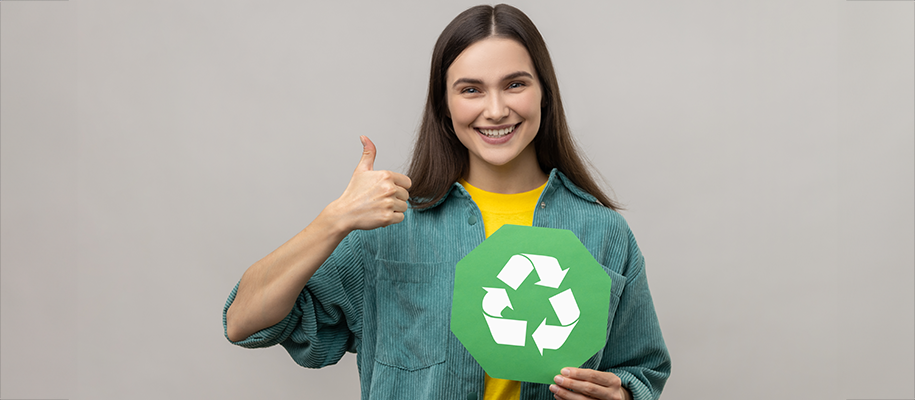 Brunette woman in corduroy shirt gives thumbs up, holds paper recycling symbol