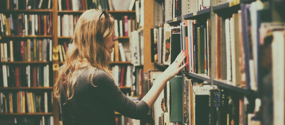 White blonde woman with sunglasses on head perusing and touching bookshelves