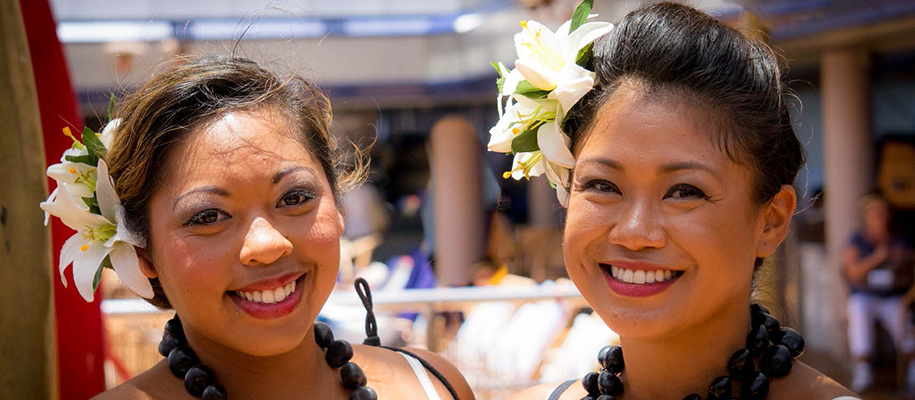 Two Pacific Islander women smiling with flowers in their hair