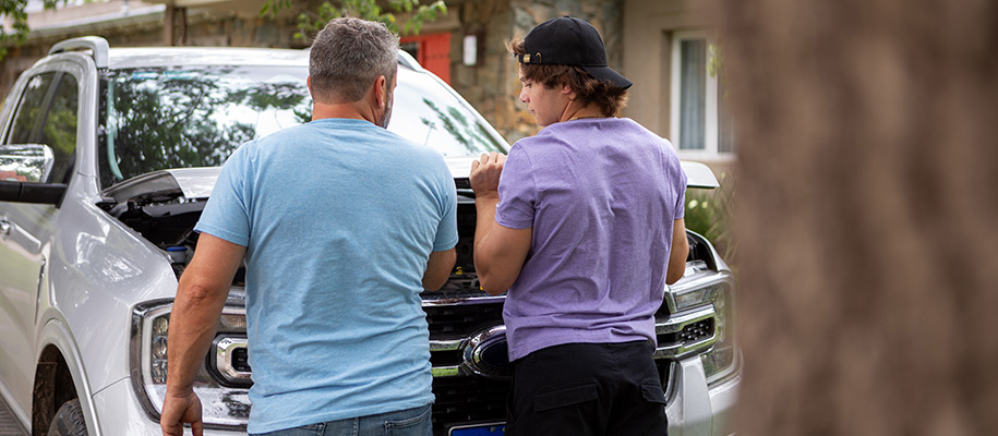 White dad and son in T-shirts popping open hood of silver car together