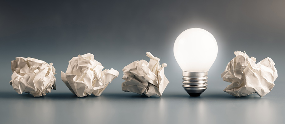 Four crumpled pieces of paper with lit lightbulb between third and fourth paper