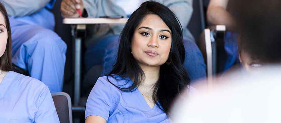 Asian woman with dark eyeliner in medical scrubs in classroom with others