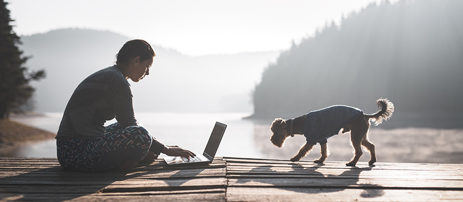 Latina teen sitting on lake pier with laptop and small dog on a misty morning