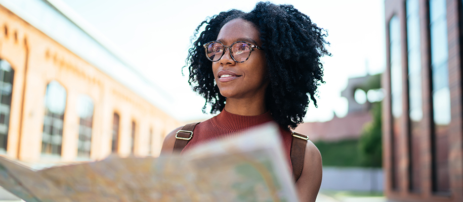Black woman with glasses looking up from map in brick and stone city