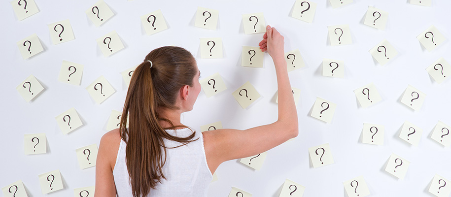 White woman back to pulling sticky note with question mark off wall of notes