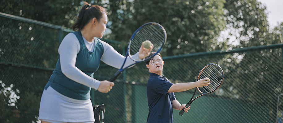 Asian woman tennis instructor teaching Asian man with down-syndrome how to serve