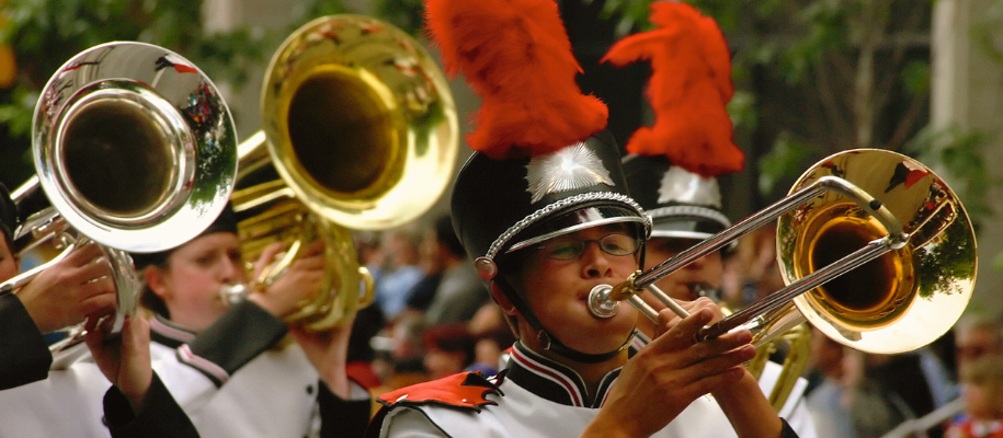 Students in black marching band hats with red feathers playing trumpets