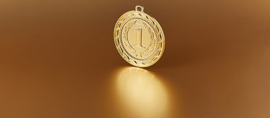 Gold award medal with one in the middle standing on end, reflection on surface