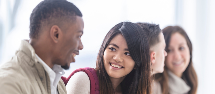 Young Asian woman with red backpack smiling at young Black man next to others