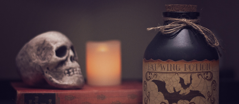 Black Bat Wing Potion jar in front of book, skull, and candle