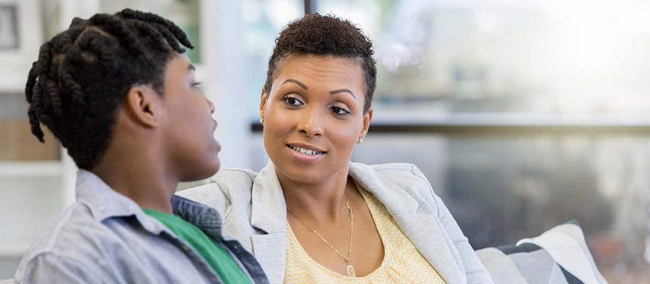 Black mother with short hair having conversation with Black son in living room
