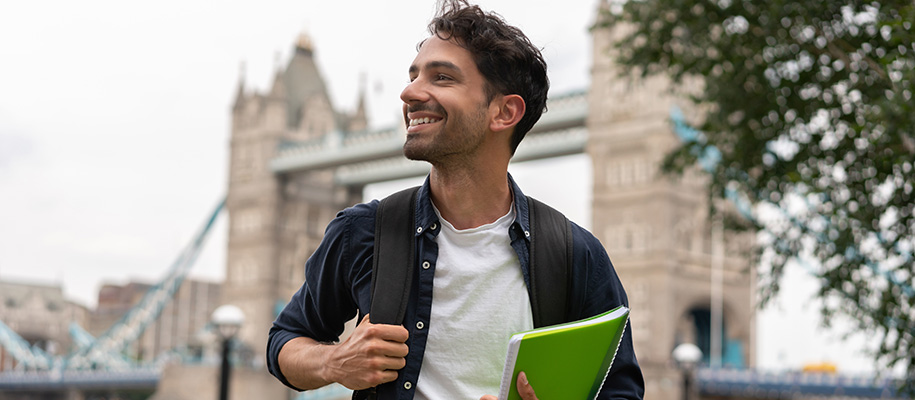 White male college student with notebook and backpack smiling in London