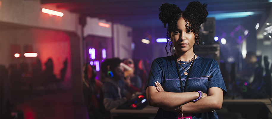 Black woman in eSports T-shirt, arms crossed, looking serious in gaming arena