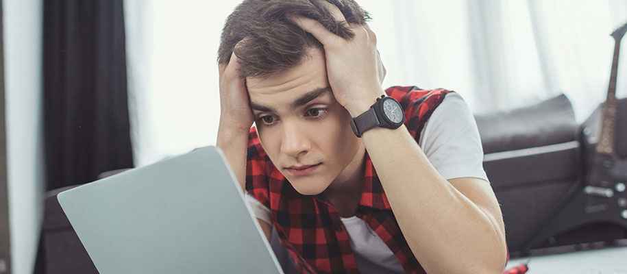 Stressed White male student looking at laptop with head in hands