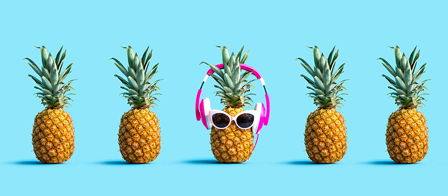 Five pineapples on blue backdrop, center one with sunglasses and headphones