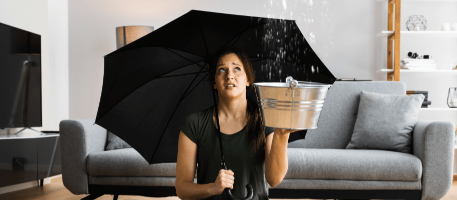 Woman holds an umbrella while catching water in a bucket dripping from ceiling