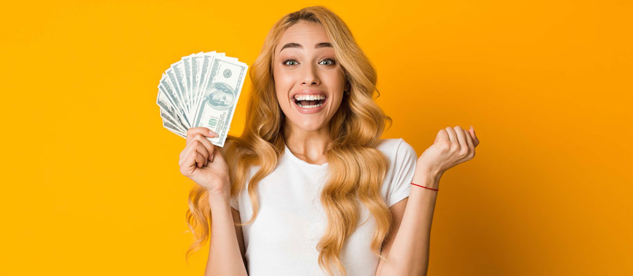 Excited blonde female holding fan of $100 bills and clenching other fist