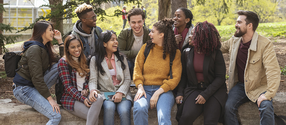 Group of diverse college students sitting on rock on campus, smiling, laughing