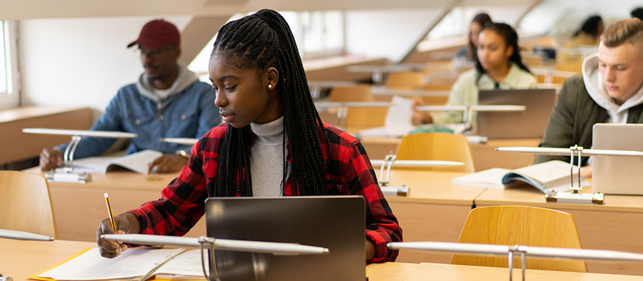 Black woman with long braids in red plaid shirt studying in busy library