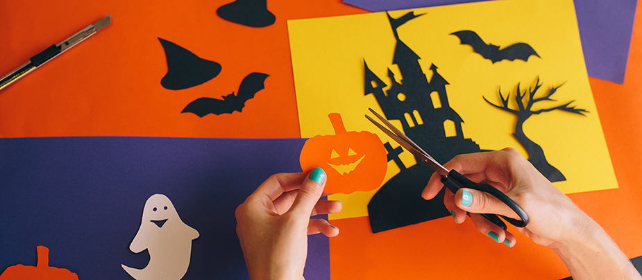 White hands cutting pumpkin over table with other cutouts, construction paper