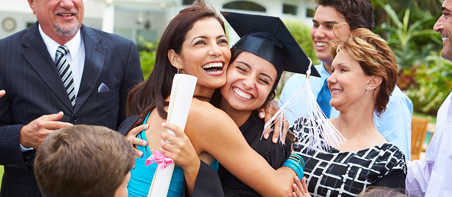 Hispanic family surrounding female graduate in black cap and gown with big smile