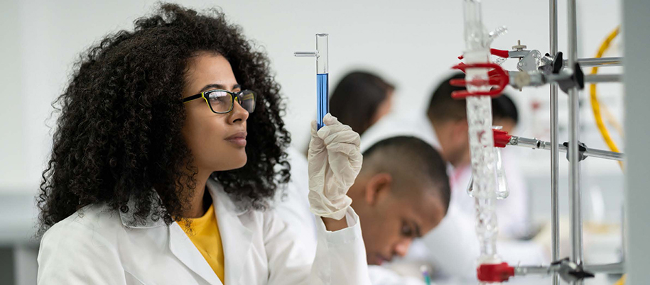 Black woman with curly hair, glasses, and tube of solution in lab with others