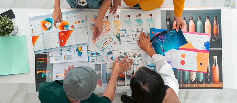 Four people leaning over table with spread of graphic design product pages