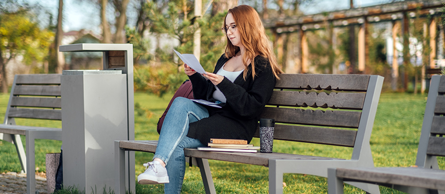 Young White woman in black sweater sitting on bench in summer reading letter
