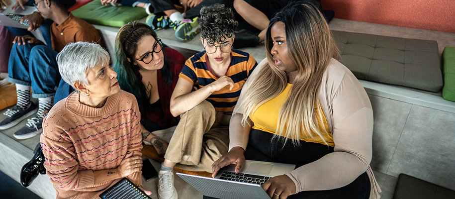 White female professor sitting in stadium seating talking to three students