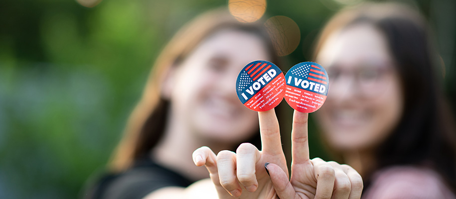 Two young women out of focus holding I Voted stickers up on fingers in focus