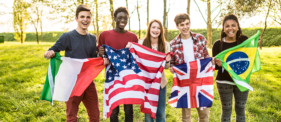 Five diverse student outside holding four country flags, smiling and laughing