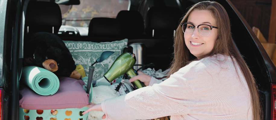 White woman with glasses, brown hair packing hairdryer into car full of stuff