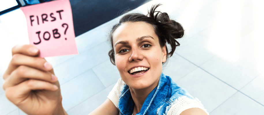 A young woman holds a post-it note that reads, "First job?"