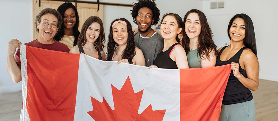 Mostly female diverse group of students in white room holding Canadian flag